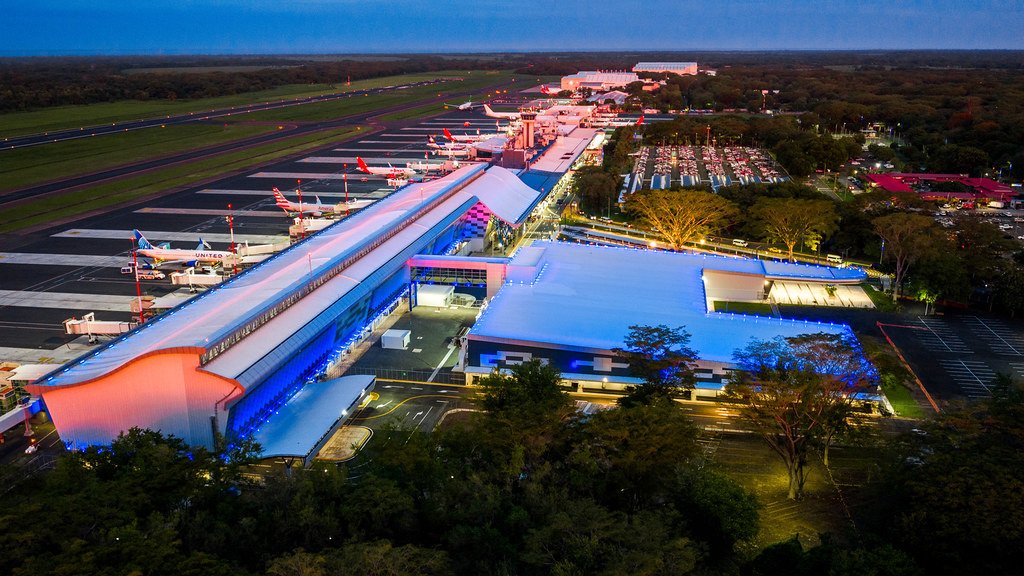 Vista aérea nocturna del Aeropuerto Internacional de El Salvador con aviones estacionados en las mangas y la terminal iluminada de azul